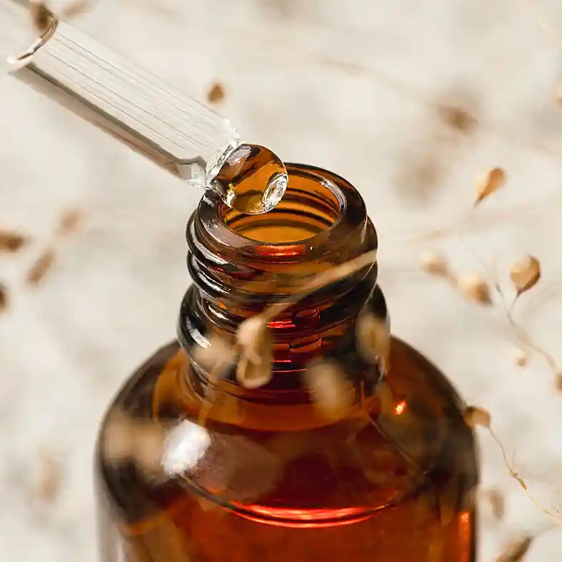 Dropper getting liquid from amber glass bottle dried grass behind it