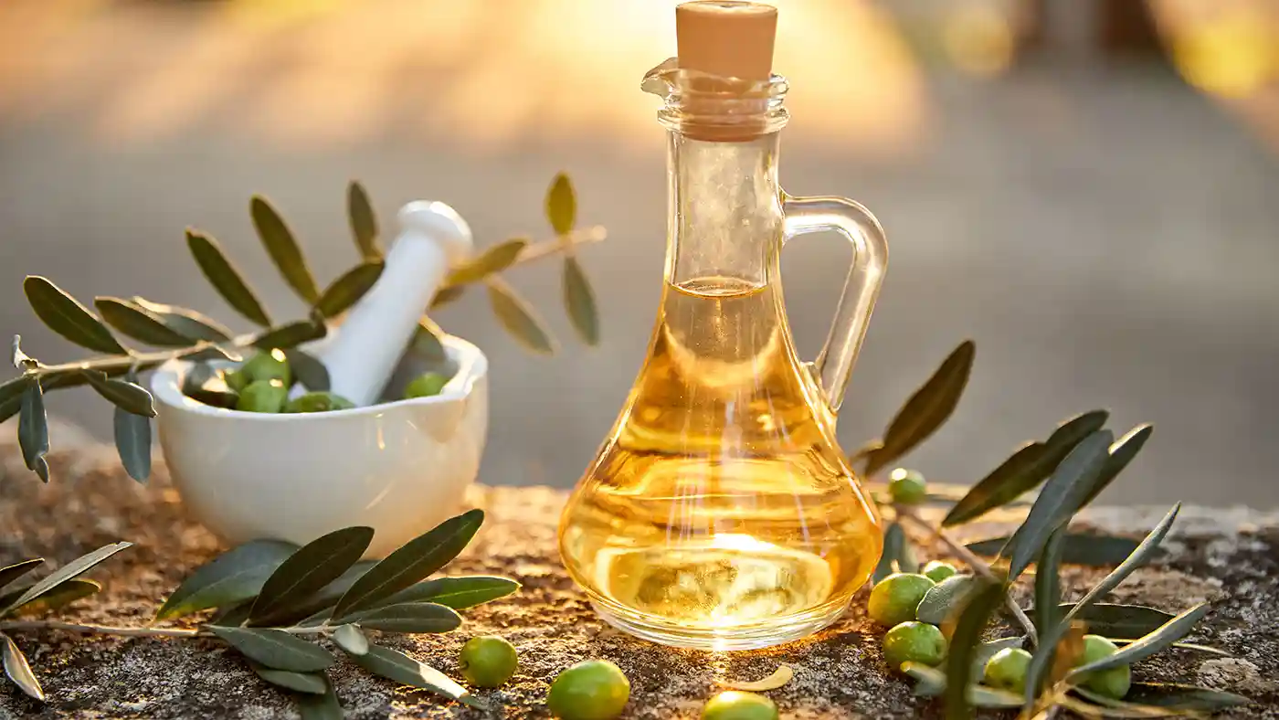 Olive branches in front of glass jug filled with oil