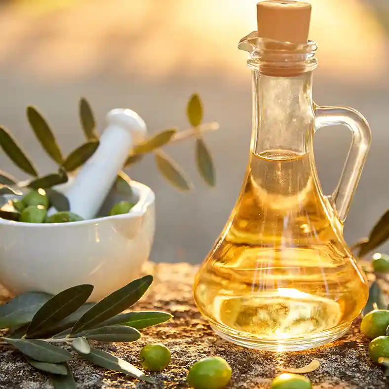 Olive branches in front of glass jug filled with oil