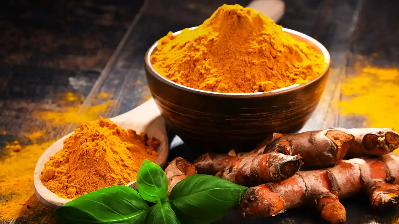 Turmeric root in front of ceramic bowl of turmeric spice